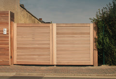 Moderne houten opritpoort van Iroko hardhout met fijne horizontale lamellen, geplaatst naast een bijpassende houten brievenbuskolom.